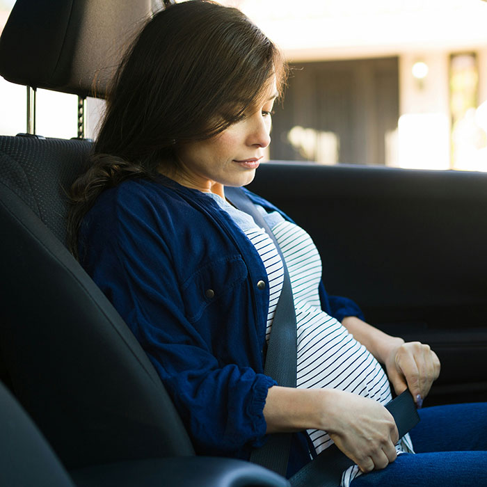 Pregnant woman in striped shirt adjusts seatbelt, illustrating weaponized incompetence scenarios in daily life.
