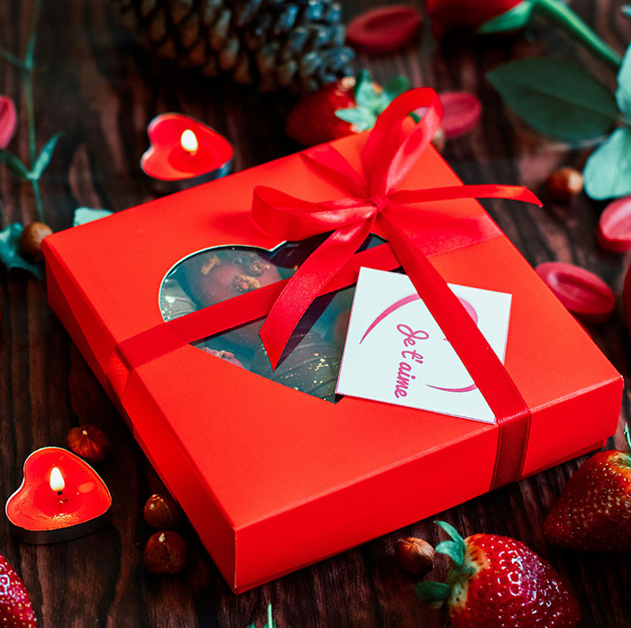 Red gift box with ribbon, surrounded by strawberries and candles, appealing items men love to receive for Valentine's Day.