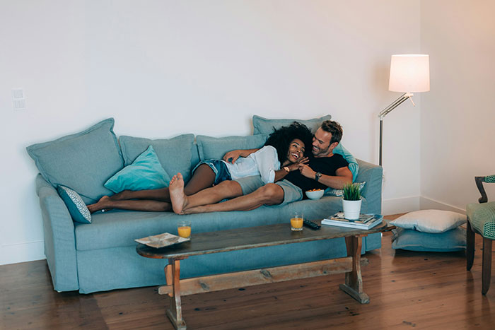 Couple relaxing on a blue sofa, surrounded by cozy decor, enjoying a moment together; guys like pretty things too.