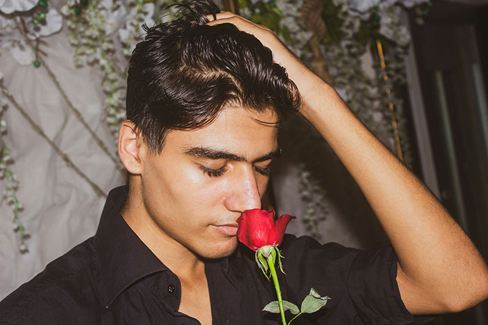 Man in a black shirt holding a red rose, symbolizing guys appreciating pretty things.