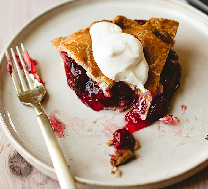 Cherry pie with whipped cream on a plate, highlighting pretty dessert options for men.