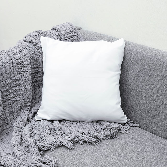 White pillow on a gray sofa with a textured blanket, representing pretty things men may like as gifts.