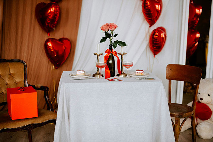 Table set for Valentine's dinner with roses, heart balloons, and a gift box.