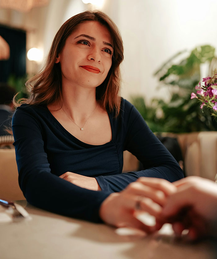A woman in a restaurant smiling, holding hands, with focus on pretty ambiance.