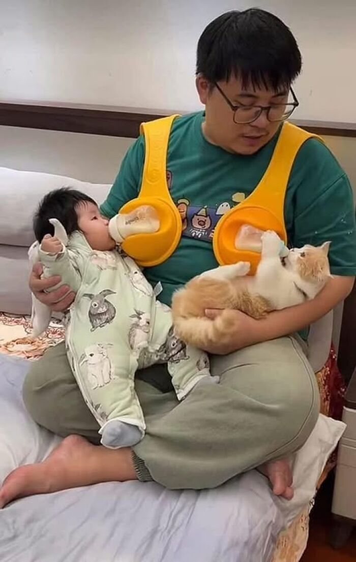 Man feeding a baby and a cat, using a bottle holder, creating a wholesome animal moment.