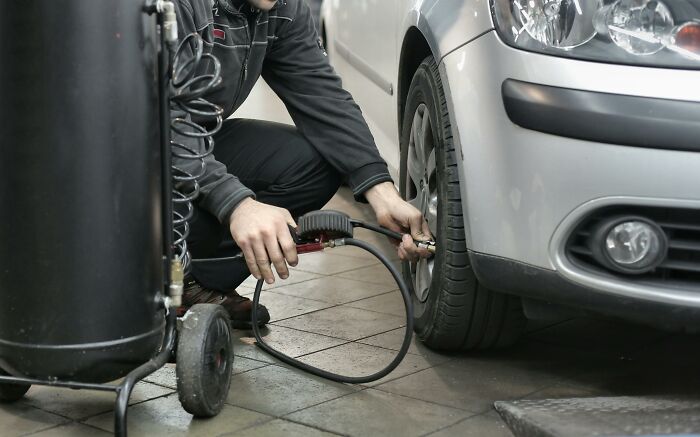 Mechanic inflating car tire with an air pump, focusing on vehicle maintenance procedures in a garage setting. Mechanic inflating car tire with an air pump, focusing on vehicle maintenance procedures in a garage setting.