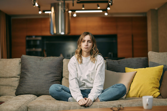 Woman sitting on a couch, looking concerned, highlighting parental financial dependence issues. Woman sitting on a couch, looking concerned, highlighting parental financial dependence issues.