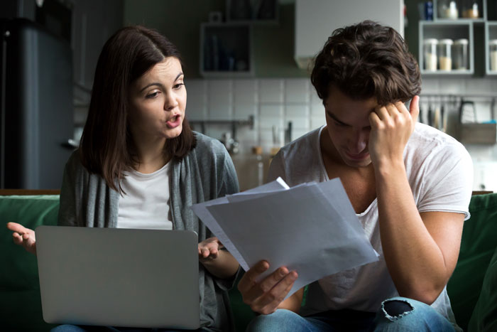 A couple having a serious discussion about finances, with a woman using a laptop and a man holding documents. A couple having a serious discussion about finances, with a woman using a laptop and a man holding documents.