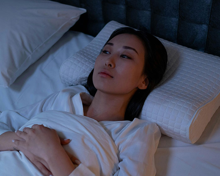 Pregnant woman looking thoughtful in bed, husband on overseas trip.