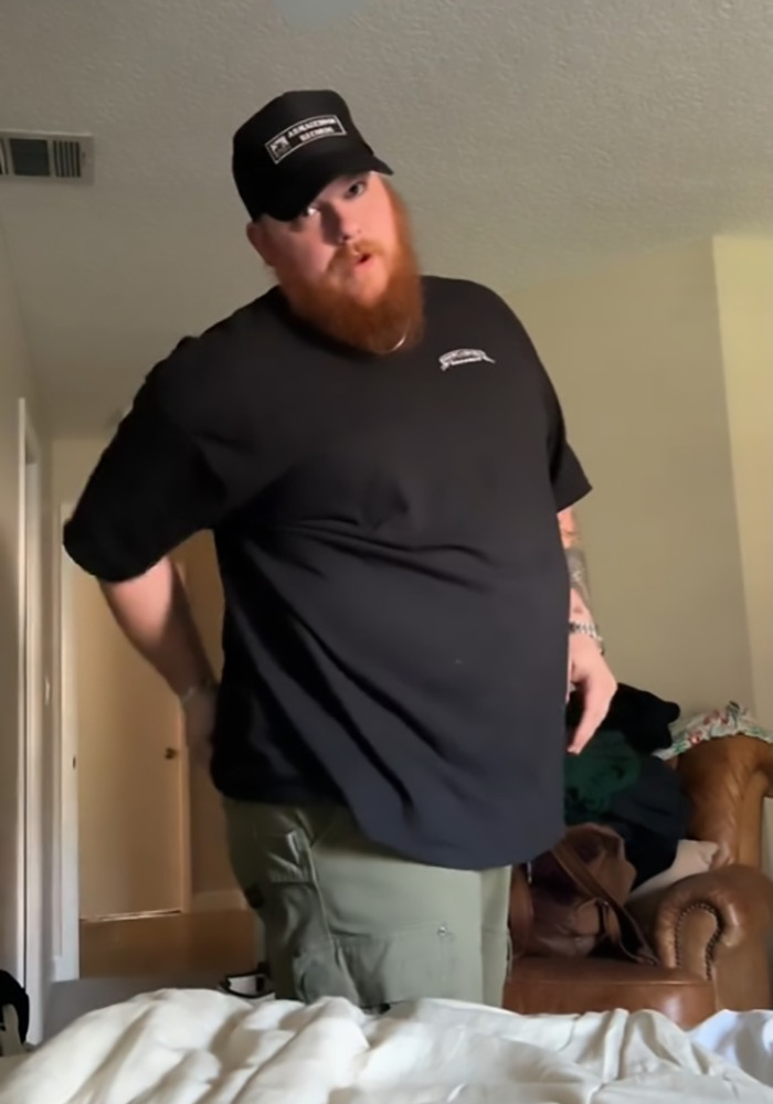 Man standing in a room wearing a black shirt and cap, illustrating a viral shower clip discussion among straight women.