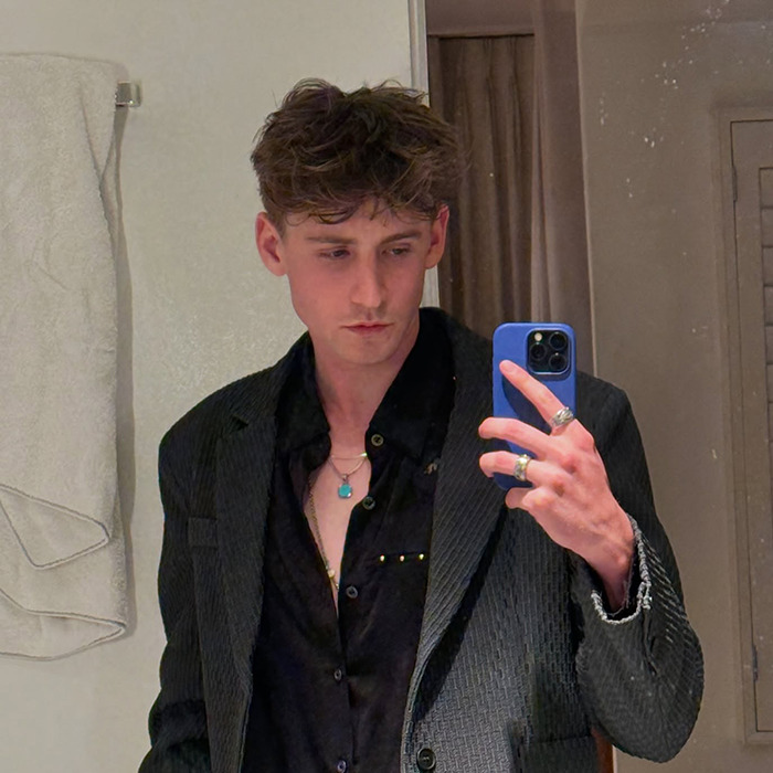 Magnus Ferrell in a black shirt and blazer taking a mirror selfie.
