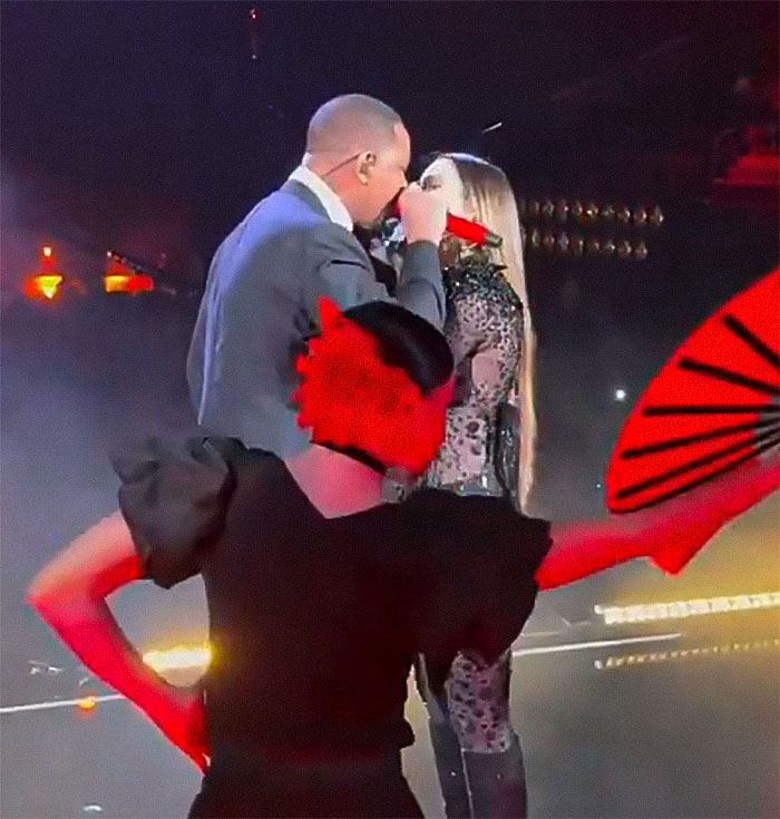 Man in a suit onstage with female singer, dramatic lighting, intense atmosphere.