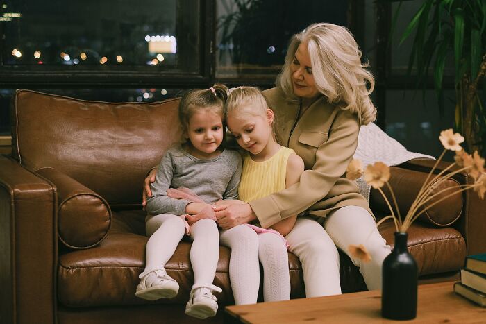 Elderly woman sharing wisdom with two young girls on a leather couch in a cozy setting.
