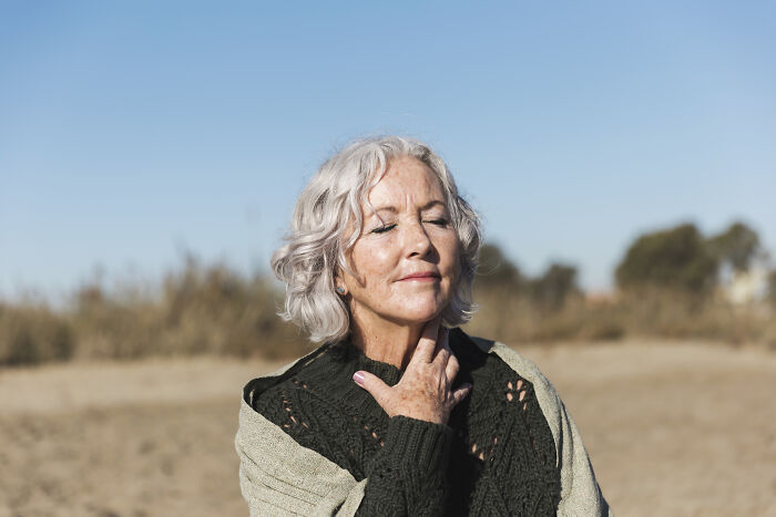 Elderly woman enjoying sunlight, embodying priceless life lessons, with closed eyes and serene expression outdoors.