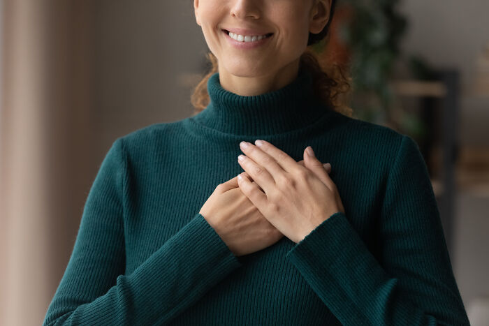 Smiling woman in a green sweater holding hands to her chest, embodying wisdom and life lessons.