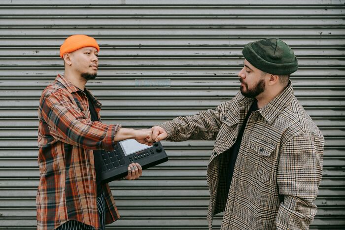 Two men in casual coats and hats sharing a fist bump in front of a metal shutter, embodying life lessons in friendship.