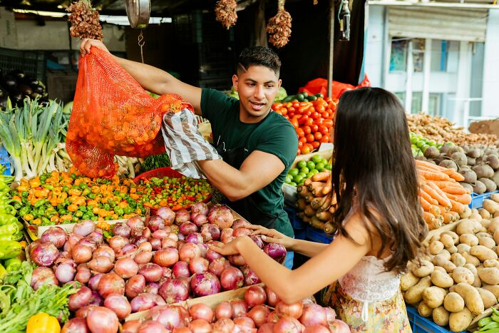 Vendor shares vegetables with customer at a vibrant market, illustrating wisdom and life lessons in everyday interactions.