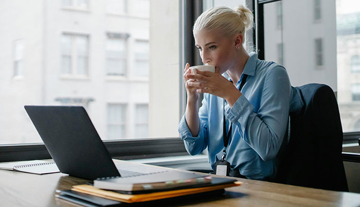Professional woman drinking coffee at work, sitting at a desk with a laptop. Professional woman drinking coffee at work, sitting at a desk with a laptop.