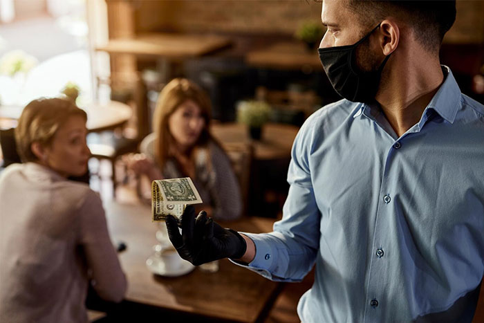 Waiter holding a dollar bill, with two women discussing something in the background at a restaurant. Waiter holding a dollar bill, with two women discussing something in the background at a restaurant.