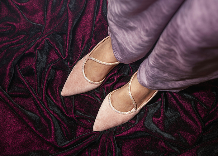 Woman wearing pink shoes standing on a purple velvet fabric.