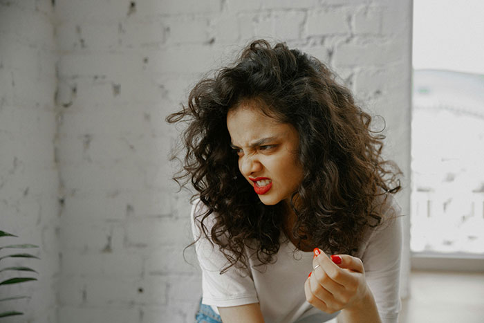 Woman making a disgusted face, sitting indoors with curly hair and a white top, enhancing the estate sale glasses theme.