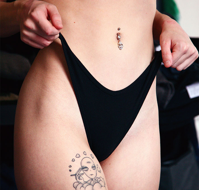 A woman with tattoo and navel piercing adjusts black underwear, related to designer genitals experience. A woman with tattoo and navel piercing adjusts black underwear, related to designer genitals experience.