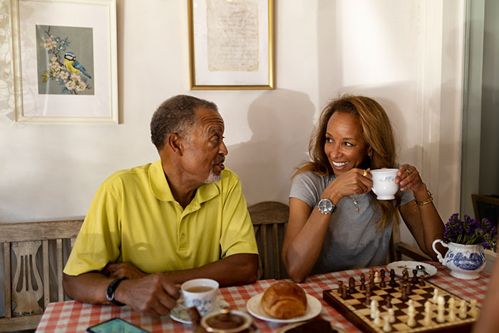 Older man and woman enjoying coffee and chatting at a table with pastries, a chessboard, and art on the wall. Older man and woman enjoying coffee and chatting at a table with pastries, a chessboard, and art on the wall.