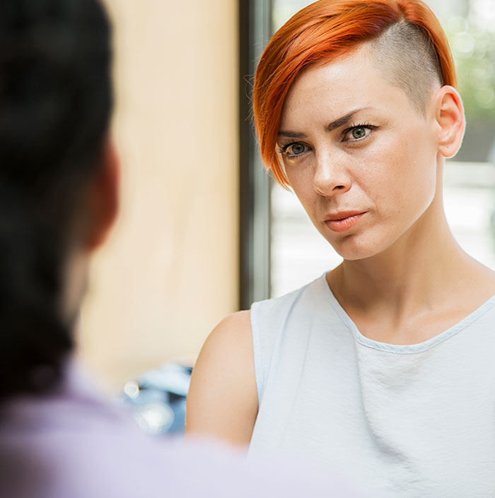 Woman with short red hair looking concerned, wearing a white shirt, represents concept of gender assumptions. Woman with short red hair looking concerned, wearing a white shirt, represents concept of gender assumptions.