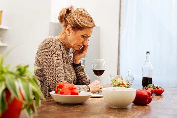 Woman sitting at dinner table with wine, looking thoughtful, surrounded by vegetables, salad, and a bottle. Woman sitting at dinner table with wine, looking thoughtful, surrounded by vegetables, salad, and a bottle.