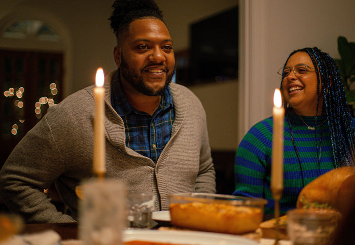 Couple enjoying dinner, candles lit, discussing a surprise birthday trip plan.