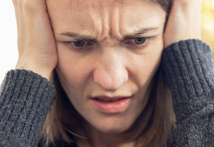 A woman looking distressed, holding her head, upset about a ruined surprise birthday trip secret for 3 months.