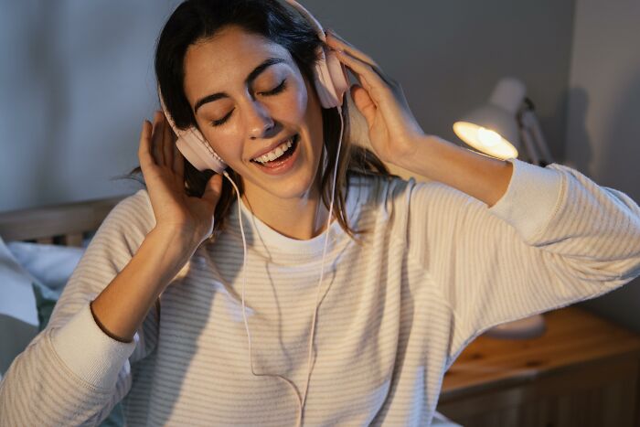 A woman in a cozy sweater smiling and listening to music with headphones, expressing love and happiness.