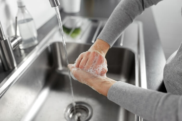 Person washing hands under a kitchen faucet, addressing everyday hygiene habits.