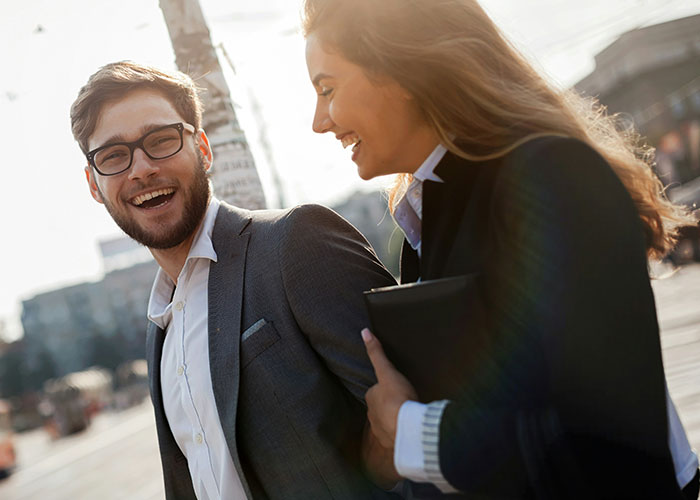 Man and woman in business attire walking and laughing, illustrating the concept of a "work wife".