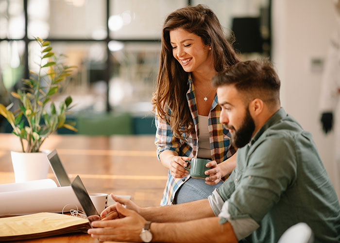 Man and woman working closely on a laptop in an office setting, illustrating the concept of a "work wife.