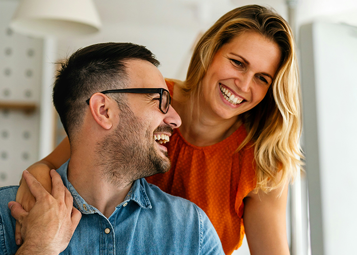 Man with smiling woman, representing work-wife scenario, both laughing indoors.