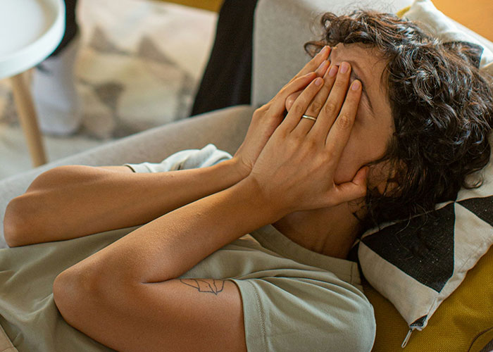 A woman feeling sad and overwhelmed, covering her face with her hands, lying on a sofa.