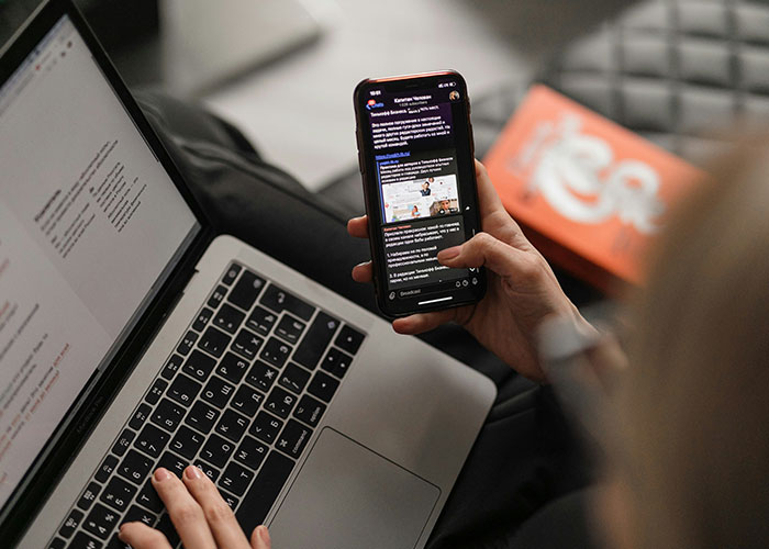 Person using a smartphone while working on a laptop, highlighting the concept of a 'work wife' in professional settings.