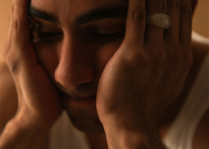Man in deep thought, resting his face in his hands, conveying the feeling of an outsider in a relationship.