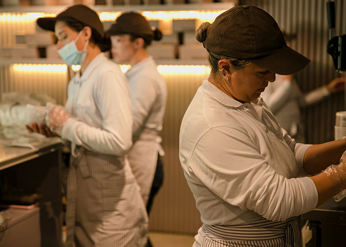 Employees in a kitchen setting, focused on tasks, wearing uniforms and caps, illustrating a toxic workplace environment scenario.