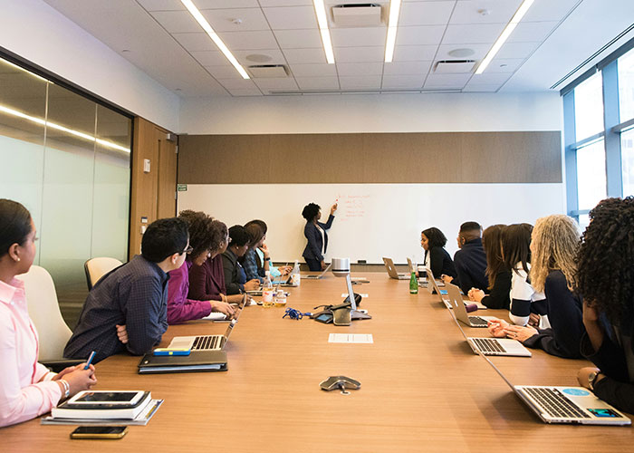 Employees in a conference room, one presenting at a whiteboard, discussing issues related to a toxic workplace.