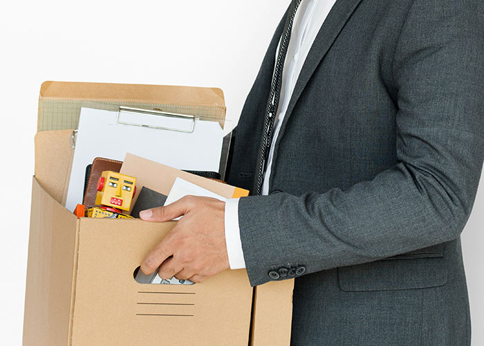 Person in a suit holding a cardboard box filled with office supplies, symbolizing quitting due to a toxic workplace.