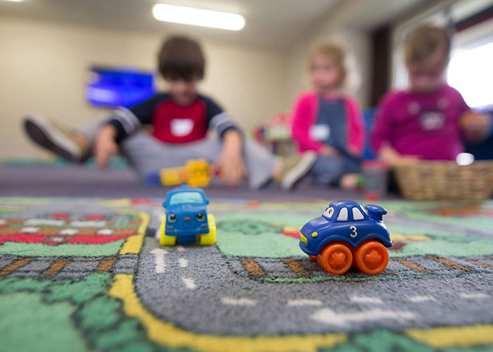 Children playing with toy cars on a carpet, focus on blue cars; illustrating a workplace setting.