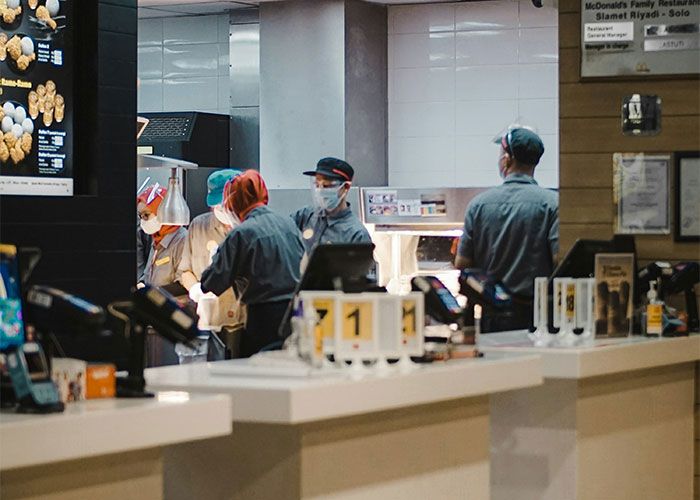 Fast food workers in uniforms and masks at a counter, highlighting a toxic workplace environment.