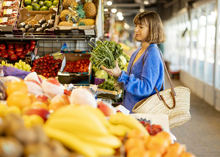 Woman shopping at a market, wearing a blue sweater, examining fresh produce.