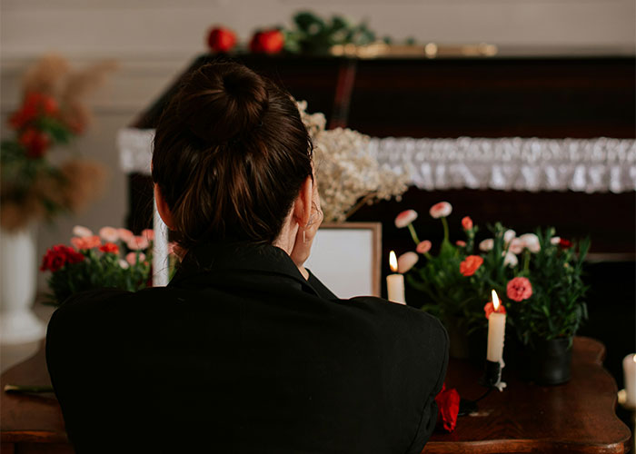 Woman in black attire facing a casket with flowers and candles, illustrating toxic workplace stress.
