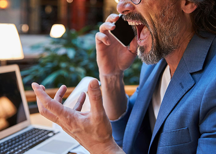 Man in a blue suit yelling on the phone, displaying workplace stress in an office setting.