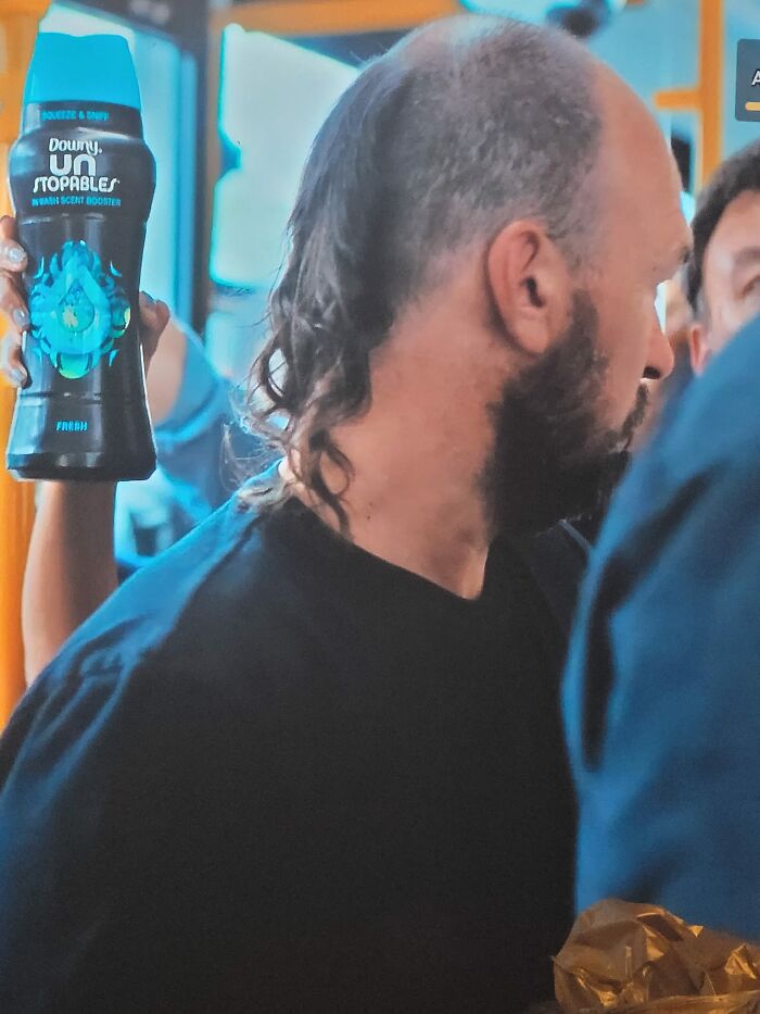 Man with a unique haircut stands while someone holds a Downy Unstopables bottle, showcasing a hair fail.