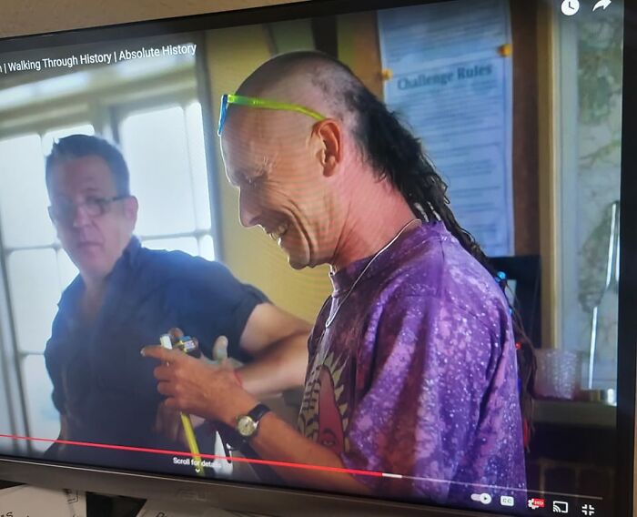 Man with a hair fail and mullet style, wearing a colorful shirt, in a casual indoor setting.