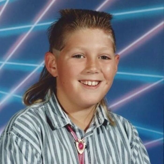 Kid with 1980s hairstyle and striped shirt, smiling in front of laser background.
